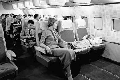 Criança dorme no colo da mãe em uma cabine de classe econômica dos 1960