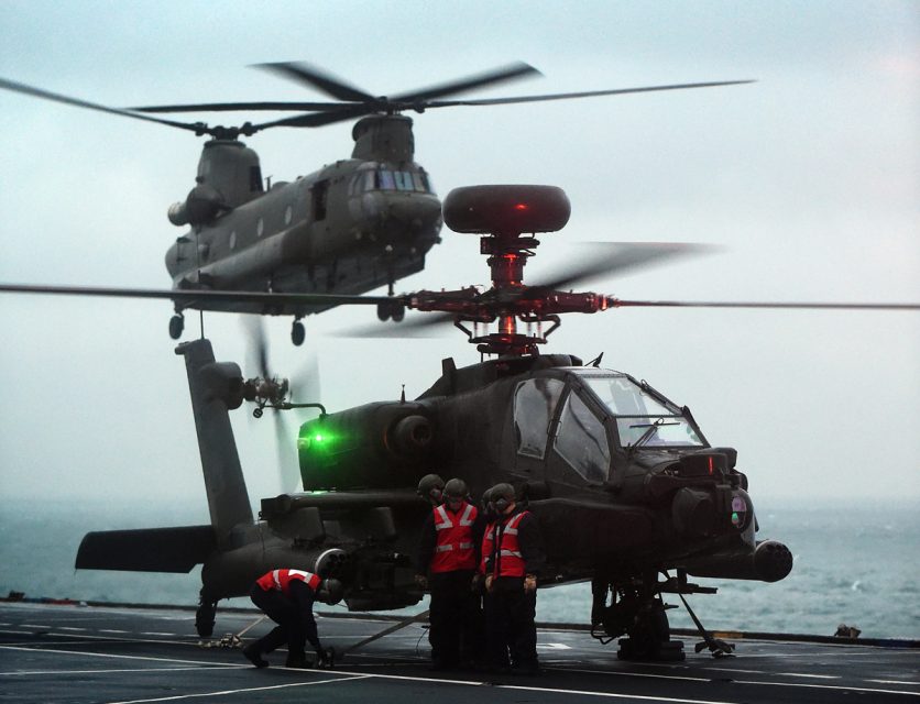 Um Apache estacionado no convés de voo do HMS Ocean; ao fundo um Chinook se aproxima (Divulgação)