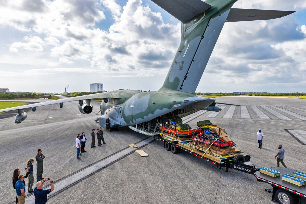 O KC-390 na famosa pista do ônibus espacial e ao fundo as estruturas para lançamento de foguetes